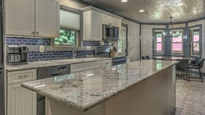 A kitchen with white cabinets, a granite countertop, a built-in oven, and a window with blinds.