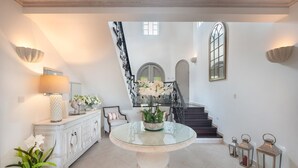 Un hall d’entrée spacieux, agrémenté d’une table ronde en verre, d’une console blanche avec une lampe, et d’un escalier menant à l’étage supérieur.