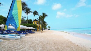 Une plage avec des chaises longues, un voilier et un bâtiment jaune.