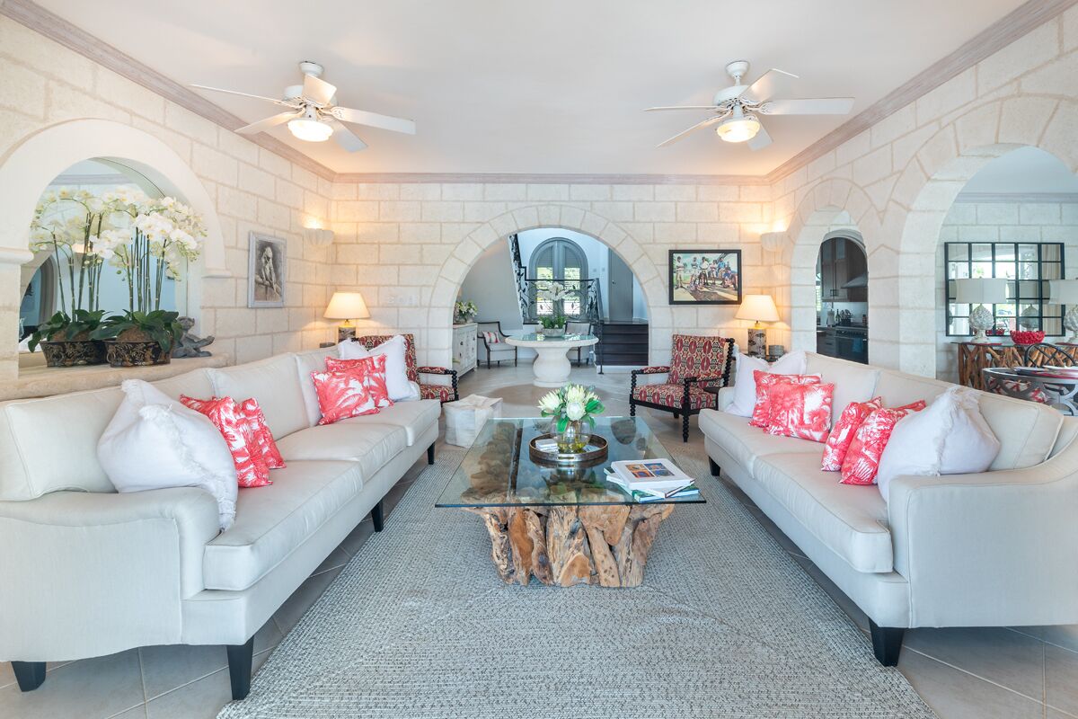 A spacious living room with two white sofas, a glass coffee table, and a ceiling fan.