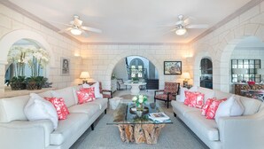 Un salon spacieux avec deux canapés blancs, une table basse en verre et un ventilateur de plafond.