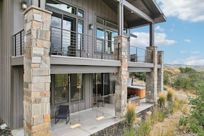 A modern two-story house with a stone exterior, large windows, and a balcony with outdoor seating.