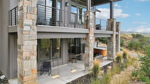 A modern two-story house with a stone exterior, large windows, and a balcony with outdoor seating.