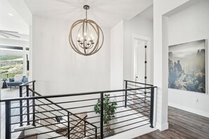 Ein modernes Interieur mit einem Kronleuchter, einer Treppe mit Geländer und einem großen Landschaftsbild an der Wand.