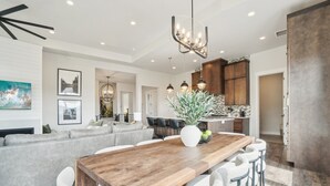 A modern kitchen with a wooden dining table, bar stools, and a vase with green apples.