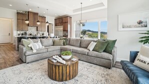 A modern living room with a sectional sofa, a round coffee table with decorative items, and a view of the outdoors.