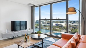 A modern living room with a large TV, a round coffee table, and a sofa. - CASSA ONE - Luxury Riverside Living in BNE CBD (Brisbane)
