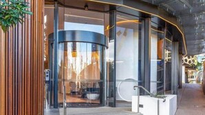 A modern building entrance with glass doors, a curved facade, and a small outdoor seating area visible through the glass. - CASSA ONE - Luxury Riverside Living in BNE CBD (Brisbane)