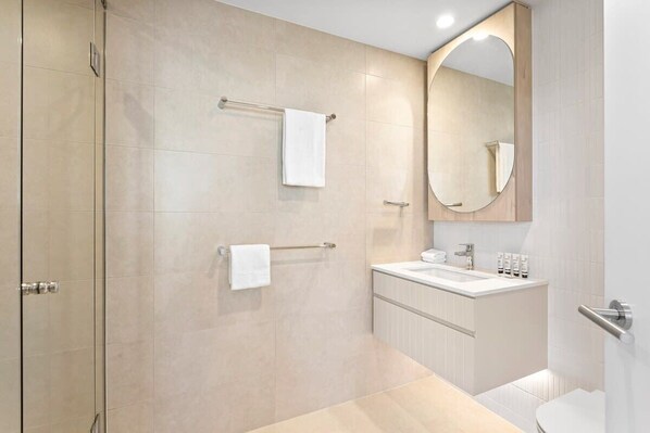 A modern bathroom with a glass shower enclosure, a white sink, and a large mirror.