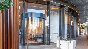 A modern building entrance with a glass facade, a curved structure, and a staircase leading inside.