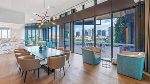Una amplia sala de conferencias con una gran mesa y sillas, ventanas grandes que ofrecen vistas a la ciudad, y un diseño moderno en el techo.