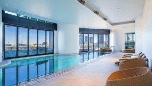 Une piscine intérieure moderne dotée de grandes baies vitrées offrant une vue sur la ville.