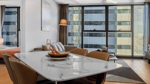Un espace repas moderne avec une table en marbre, des chaises en cuir et une vue sur le paysage urbain grâce à de grandes fenêtres.