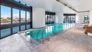 A modern indoor swimming pool with large windows offering city views.