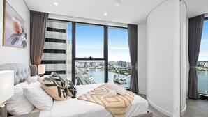 A modern bedroom with a large bed, a city view, and a cityscape visible through the window.
