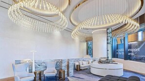 A modern lobby with a circular reception desk, seating area, and a large chandelier.