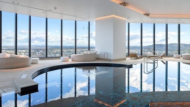 Une piscine intérieure moderne à débordement, offrant une vue panoramique sur la ville, de grandes fenêtres et un mobilier minimaliste.