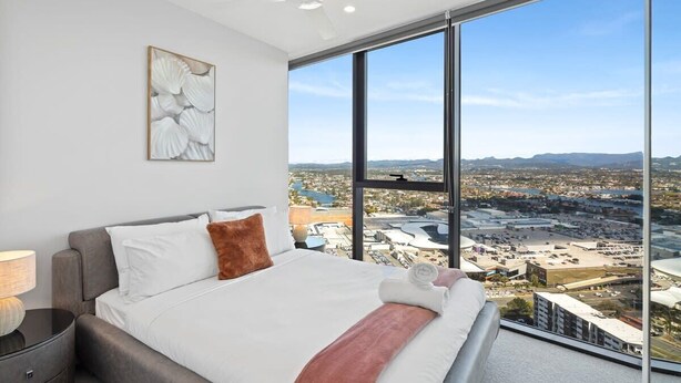 A modern bedroom with a large bed, a ceiling fan, and a city view through floor-to-ceiling windows. - CASSA CASINO - Spectacular River & Hinterland Views 1 Bed Apt in Broadbeach! (Broadbeach)