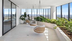 A modern balcony with hanging wicker chairs, large windows, and a view of the city. - CASSA CASINO - Spectacular River & Hinterland Views 1 Bed Apt in Broadbeach! (Broadbeach)