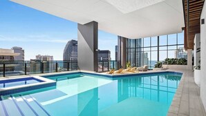 A rooftop infinity pool with lounge chairs and a city view.