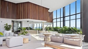 A modern indoor lounge with a high ceiling, large windows, and a variety of seating arrangements including sofas, chairs, and tables.