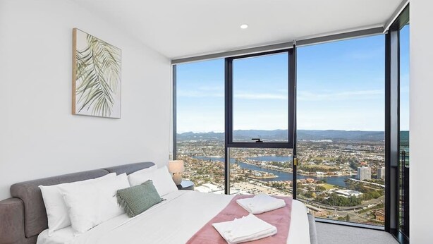 A modern bedroom with a large bed, a view of a cityscape through floor-to-ceiling windows, and a city skyline view.