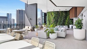 A rooftop lounge with outdoor seating, a vertical garden wall, and a city skyline view.