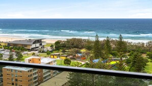 A coastal view with a beach, ocean, and a residential area with buildings and greenery.