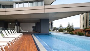 A modern building with a rooftop pool area, featuring lounge chairs and a clear view of the surrounding cityscape.