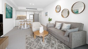 A modern living room with a grey sofa, a wooden coffee table, and a dining area with white chairs.