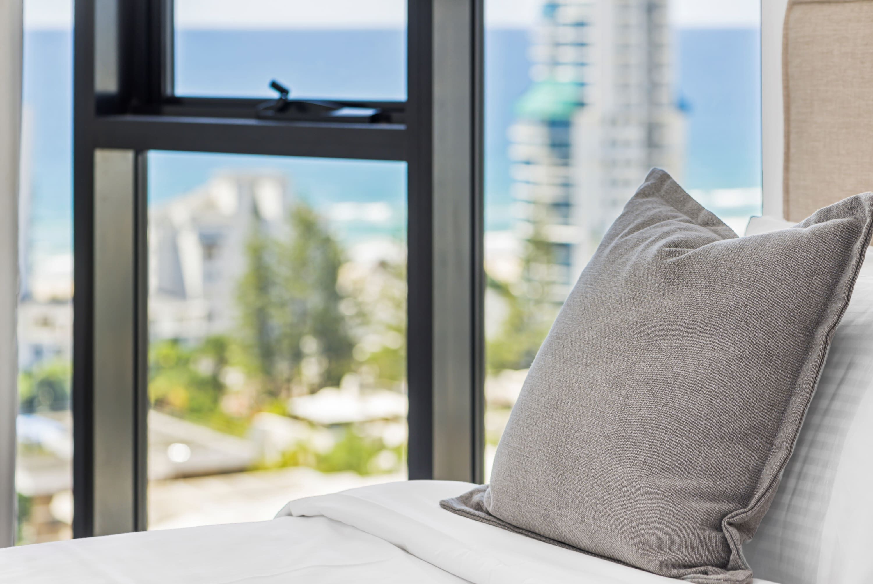 A bed with a pillow and a view of a cityscape through a window.