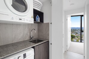 A modern kitchen with a built-in washing machine, a sink, and a view of a cityscape through a balcony.