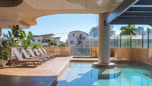 Una piscina en la azotea con sillones de descanso y vistas de edificios circundantes.