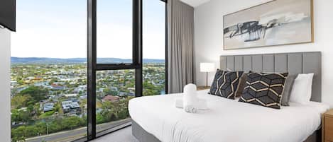 Habitación de hotel con una cama grande, vistas a un paisaje urbano, un cuadro en la pared y una lámpara en la mesita de noche.