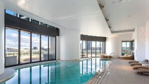 Una piscina interior moderna con paredes de vidrio transparente y vistas a la ciudad.