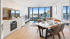 Una cocina moderna con vistas a la ciudad, un comedor con mesa puesta para cuatro, y una sala de estar con sofá y televisor.