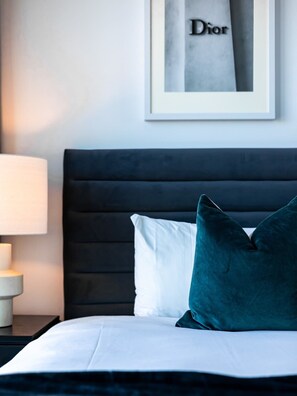 A neatly made bed with white and teal pillows, a dark headboard, and a framed sign on the wall.