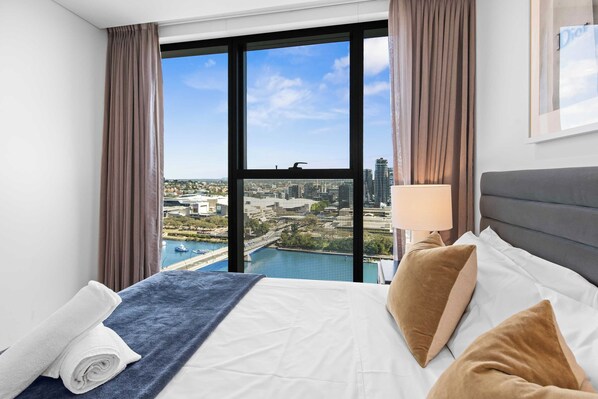 A hotel room with a large bed, a view of a cityscape, and a window with curtains.