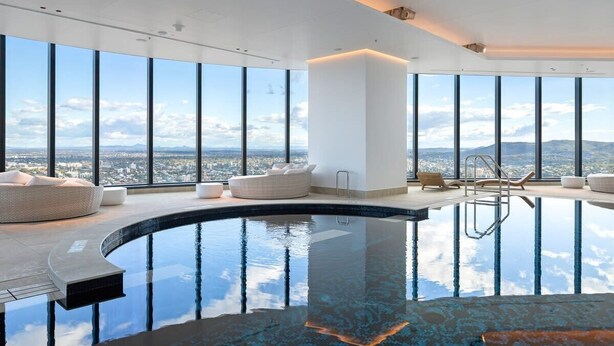 Una piscina infinita moderna en interior con vistas panorámicas de la ciudad, amplias ventanas y mobiliario minimalista.