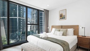Ein modernes Hotelzimmer mit großem Fenster, einem ordentlich bezogenen Bett, einer Bank und einem Nachttisch.