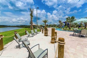 Un espace aménagé au bord de la piscine, avec des chaises longues, une piscine, des palmiers et une vue sur une étendue d’eau.