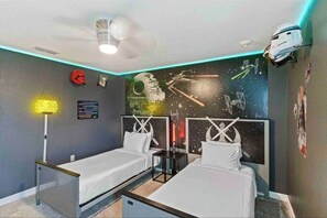 Une chambre avec deux lits, une fresque murale sur le thème de Star Wars et un projecteur au plafond.