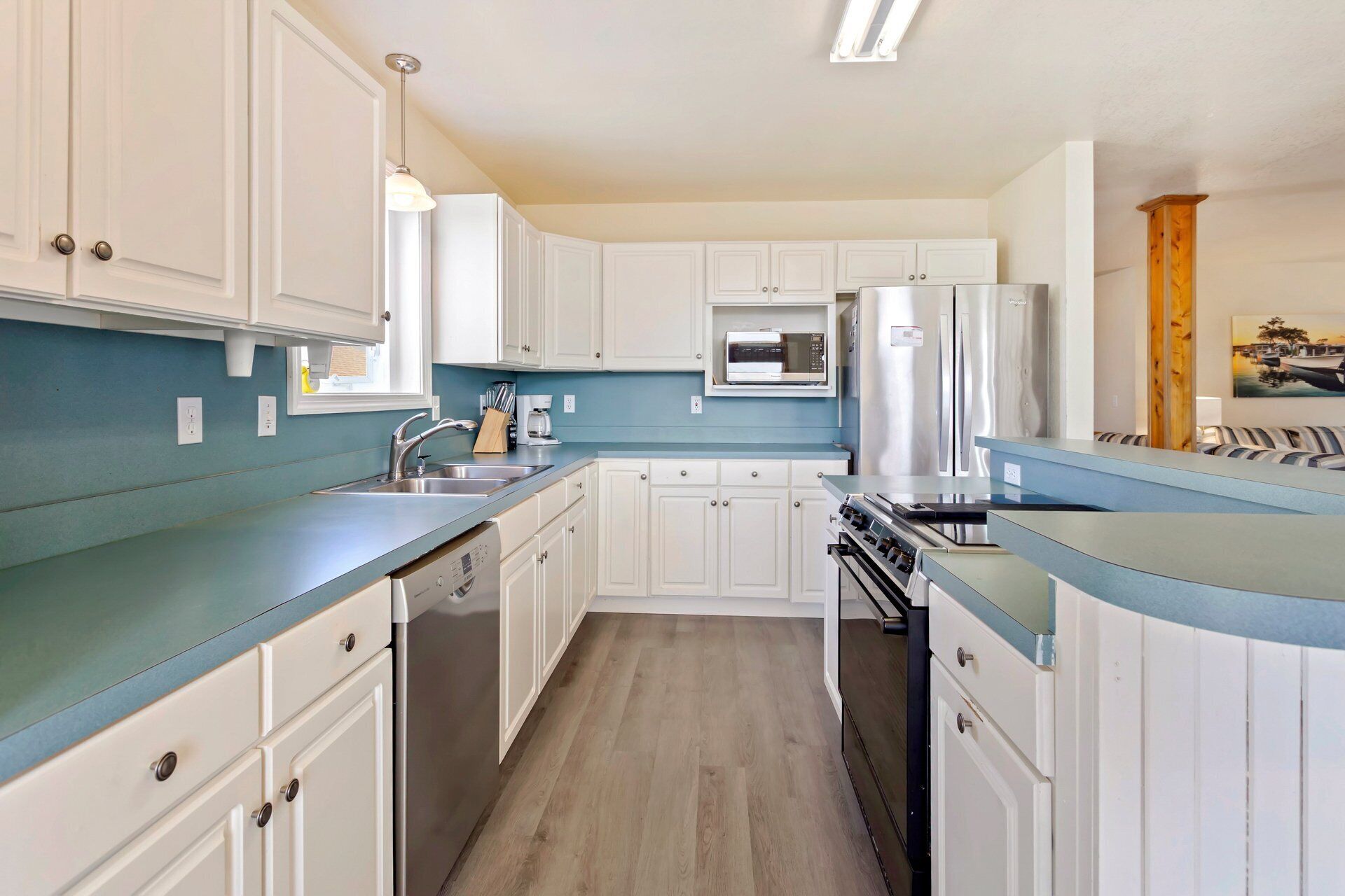 Una cocina con armarios blancos, encimera azul, refrigerador de acero inoxidable y microondas.