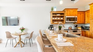 Uma cozinha moderna com armários de madeira, bancada de granito e um espaço de refeições com mesa e cadeiras redondas.