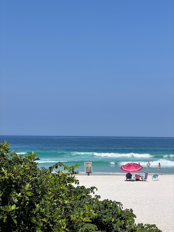 Ein Strand mit blauem Himmel, Wellen im Meer und ein paar Personen.