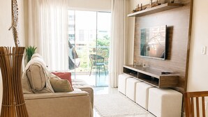 A modern living room with a sofa, TV, and a dining area. - Confortável Apto na Praia do Forte (Cabo Frio)