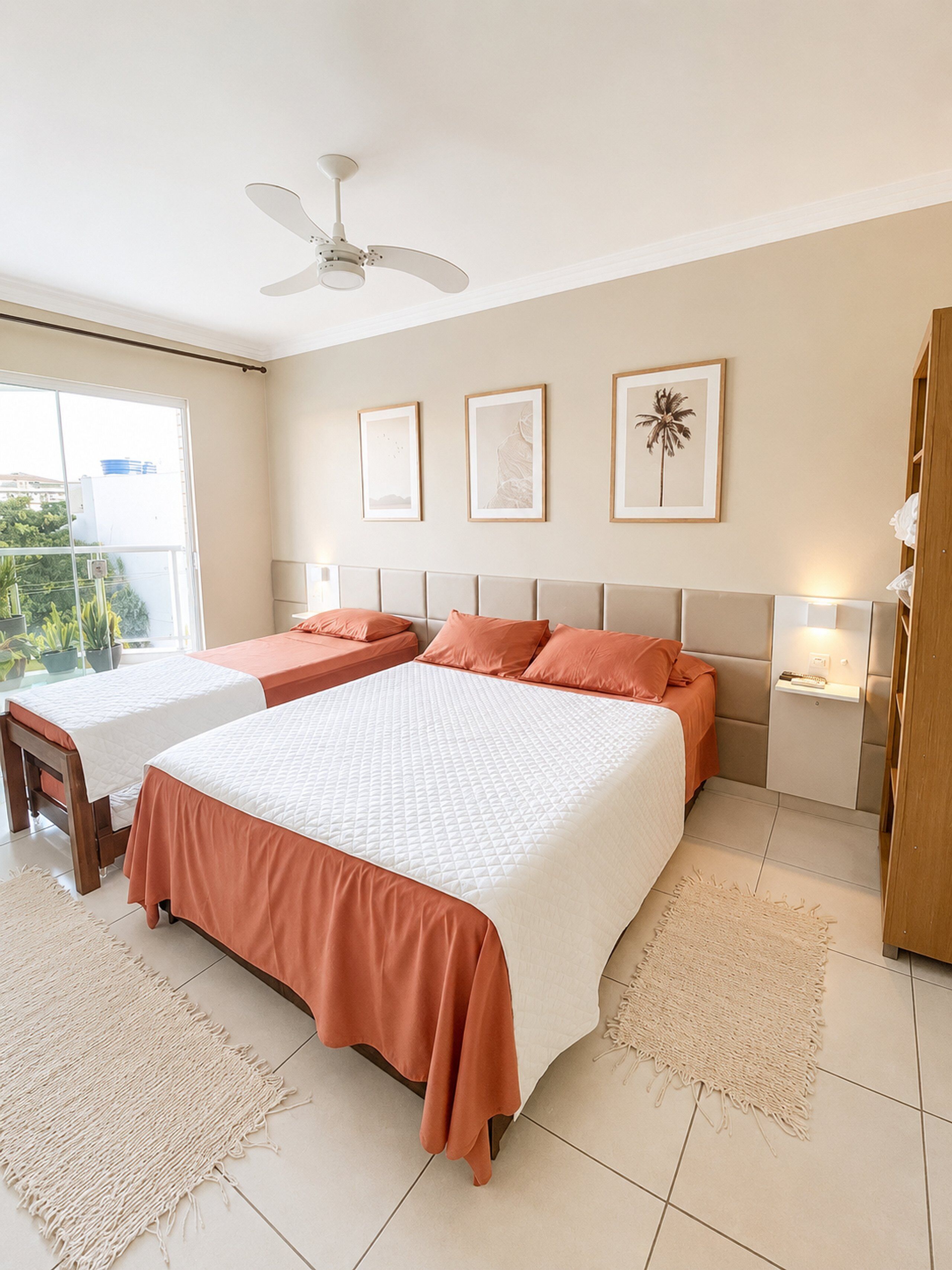 A hotel room with two beds, a ceiling fan, a large window, and framed artwork on the wall.