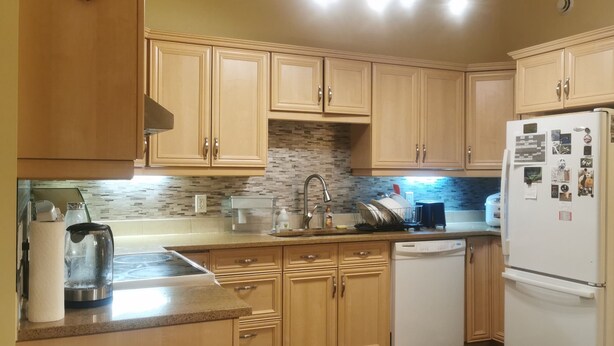 A kitchen with wooden cabinets, a microwave, a dishwasher, and a refrigerator. - Grant's Arctic Escape (Iqaluit)