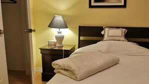 A neatly made bed with a white comforter and pillows, a bedside lamp, and a nightstand with a tissue box. - Grant's Arctic Escape (Iqaluit)