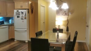 A compact kitchen with wooden cabinets, a white refrigerator, and a dining table with chairs. - Grant's Arctic Escape (Iqaluit)